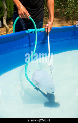 Nahaufnahme eines jungen kaukasischen Mann Reinigen der Unterseite eines tragbaren Pool im Hinterhof mit einem manuellen Pool Cleaner Stockfoto