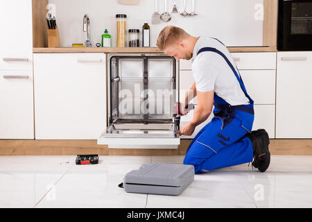 Junge Handwerker Service Arbeitnehmer Reparatur Geschirrspüler Gerät in der Küche Stockfoto