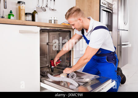 Junge Handwerker zur Festsetzung Spülmaschine mit elektrischen Bohrmaschine Stockfoto