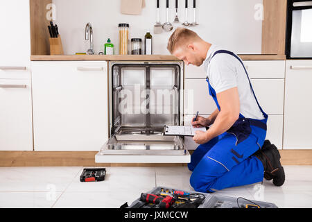 Handwerker in der Nähe Spülmaschine schriftlich über die Zwischenablage in der Küche Stockfoto