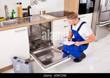 Handwerker in der Nähe Spülmaschine schriftlich über die Zwischenablage in der Küche Stockfoto