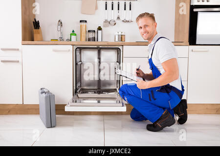 Handwerker in der Nähe Spülmaschine schriftlich über die Zwischenablage in der Küche Stockfoto