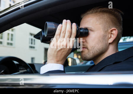 Privatdetektiv Sitzen im Auto durch Fernglas Stockfoto