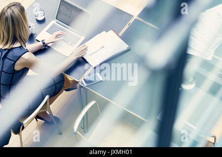 Hohen winkel Fenster mit Blick auf junge geschäftsfrau Tippen auf Laptop im Büro Schreibtisch Stockfoto