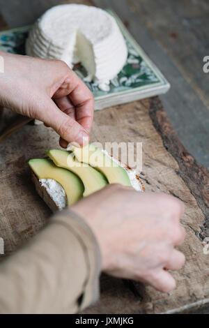 Frau Inverkehrbringen Scheiben Avocado auf geschnittenes Brot mit Ricotta, close-up Stockfoto