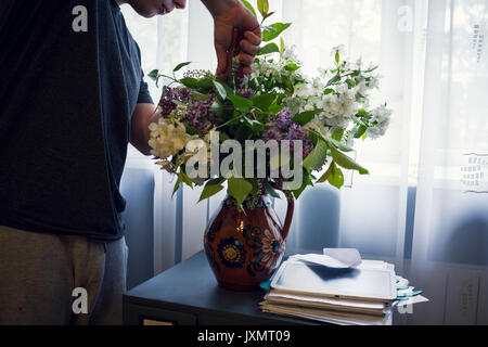 Den mittleren Abschnitt des jungen Mannes, die Vase mit Blumen vor dem Fenster Stockfoto