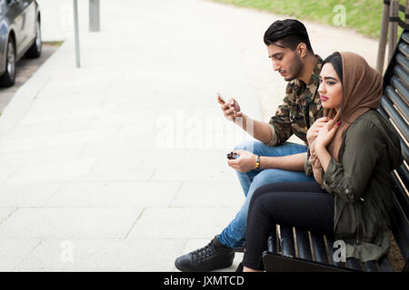 Junges Paar sitzen auf der Parkbank, junge Mann an Smartphone suchen Stockfoto