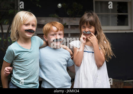 Kinder tragen von gefälschten Schnurrbärten auf Kamera lächeln Stockfoto