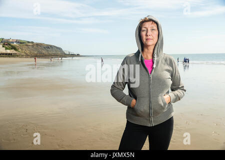 Frau am Strand in Kapuzenoberteil, Folkestone, Großbritannien Stockfoto