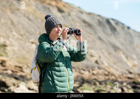 Frau mit Fernglas auf Fels, Folkestone, Großbritannien Stockfoto