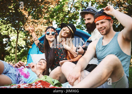 Fünf junge erwachsene Freunde spielen akustische Gitarre während Festival Camping Stockfoto