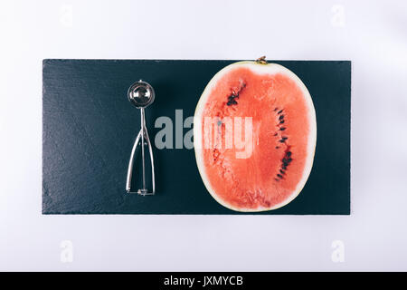 Hälfte eine reife Wassermelone und ein Löffel für Speiseeis auf einem weißen Tisch Ansicht von oben Stockfoto