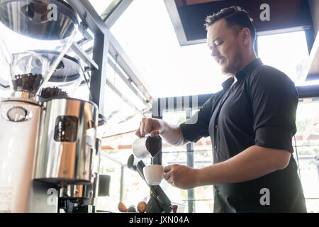 Ernsthafte Barkeeper gießen frische Milch in eine Tasse Kaffee in einer t Stockfoto