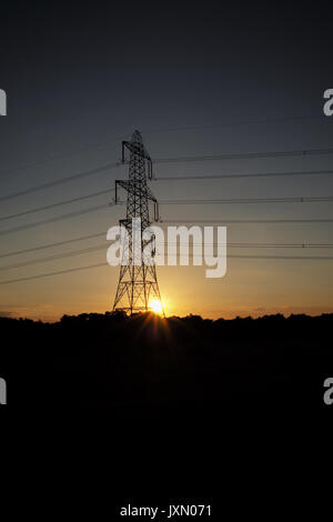 Die Sonne stellt neben einem Strom pylon verlässt den Turm gegen einen orange sky Silhouette Stockfoto