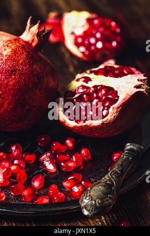 Geöffnet Granatapfel und Ganzen mit Samen auf Metallplatte und Vintage Messer. Vertikale Ausrichtung. Stockfoto