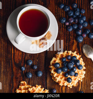 Weiße Tasse Tee mit Blaubeeren und Belgische Waffeln auf Holz- Hintergrund. Blick von oben. Stockfoto