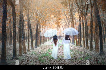 Vietnamesisches Mädchen in traditionellen langen Kleid oder Ao Dai Holding umbrella Tunika fahren Sie Richtung Ende der Strasse im Wald auf einem sonnigen Sommertag in Dong Nai, Vietnam Stockfoto