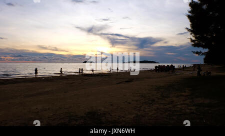 Ein Strand bei Sonnenuntergang, mit Silhouette von Menschen spielen am Strand und die Aussicht genießen. Entfernte Inseln im Hintergrund. Bunte orange Stockfoto