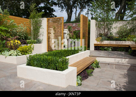 Ein Ausstellungsgarten mit geschlitzten Holztoren, Bänken und abgeschnittenen Hecken in Southport, Merseyside, Großbritannien, im Jahr 2017. Es verfügt über einen modernen, modernen Gartenraum im Innenhof, erhöhte Grenzen, Terrassenbereiche und Wasser. Am letzten Tag der Vorbereitungen für die Flower Show verleihen Aussteller, Gartendesigner und Blumenkünstler den letzten Schliff der Ausstellungen, die die Besucher dieser berühmten jährlichen Veranstaltung begeistern werden. Stockfoto