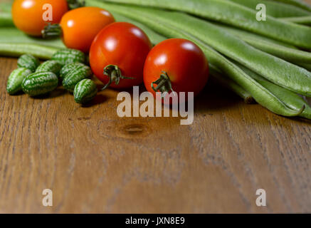 Cucamelons, orange und rote Tomaten in selektiven Fokus gegen frische grüne Stangenbohnen auf Holz mit Kopie Raum Stockfoto