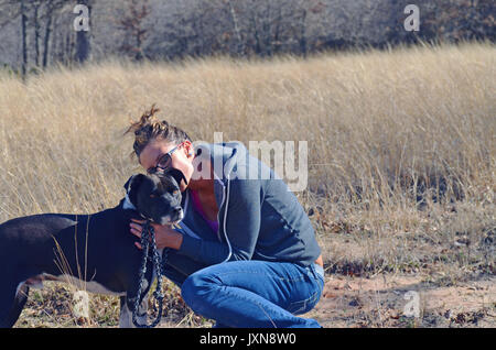 Mädchen und Fell Baby spielen in das Feld ein. Annahme durch den schwarzen und weißen Hund empfängt Umarmen und Küssen von Familie. Stockfoto