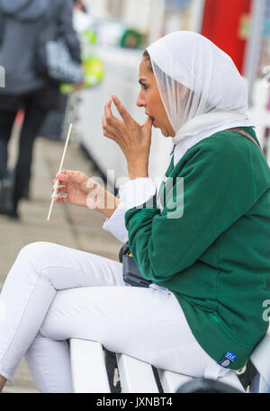 Junge asiatische Frau sitzen unten lecken sich die Finger beim Essen essen in Großbritannien. Stockfoto