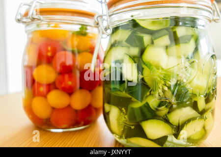 Lacto-fermentierten Gemüse. Glas Gläser auf hölzernen Küchentisch mit hellen Hintergrund. Tomaten und Gurken fermentiert, vegetarisches Essen Konzept. Stockfoto