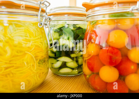 Lacto-fermentierten Gemüse. Glas Gläser auf hölzernen Küchentisch mit hellen Hintergrund. Tomaten, Zucchini (Zucchini) und Gurke fermentiert. Stockfoto