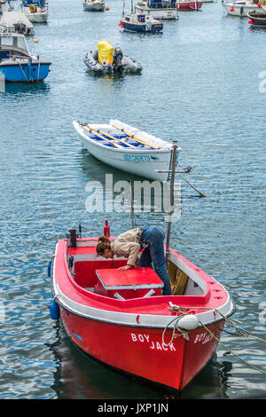 Eine Frau mittleren Alters, allein in ein kleines Motorboot, das Sie zu Moor, unter anderem Boote im Hafen von Penzance, Cornwall, England, Großbritannien. Stockfoto