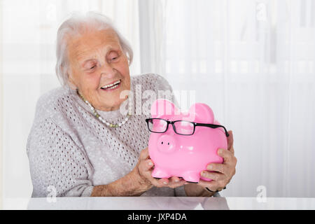 Gerne ältere Frau mit Sparschwein zu Hause Stockfoto