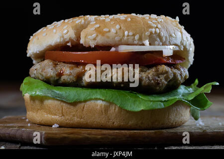 Rolle mit gebratenem Schnitzel. Hamburger auf ein Holzbrett. Küchentisch, schwarzen Hintergrund. Stockfoto
