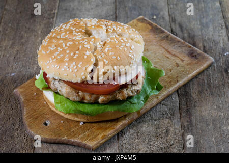 Rolle mit gebratenem Schnitzel. Hamburger auf ein Holzbrett. Küchentisch, schwarzen Hintergrund. Stockfoto