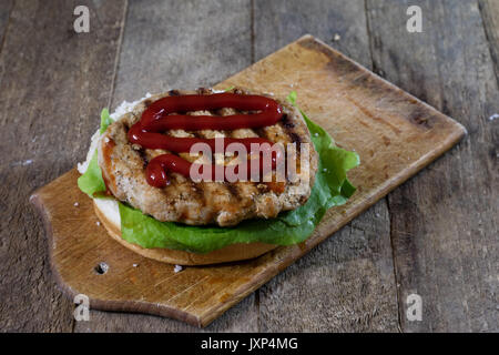 Rolle mit gebratenem Schnitzel. Hamburger auf ein Holzbrett. Küchentisch, schwarzen Hintergrund. Stockfoto