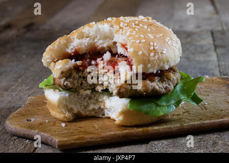 Rolle mit gebratenem Schnitzel. Hamburger auf ein Holzbrett. Küchentisch, schwarzen Hintergrund. Stockfoto
