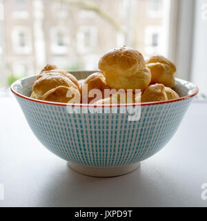 Seitenansicht des Windbeutel in eine blaue gepunktete Schüssel auf einem weißen Tisch. Quadratisches Format. Stockfoto