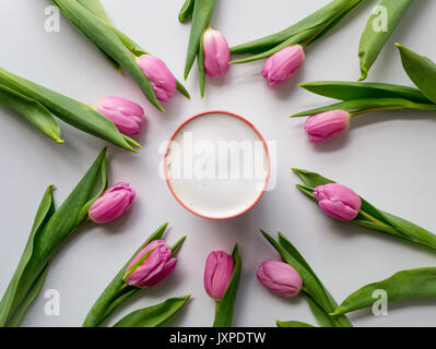 Rosa Tulpen im Kreis auf einem weißen Tisch mit einem Cappuccino Tasse in der Mitte angeordnet. Flach. Querformat. Stockfoto