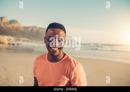 Afro-amerikanische Mann stand am Strand und lächelnd. Horizontale Schuß von positiven jungen Kerl, der am Ufer des Meeres. Stockfoto