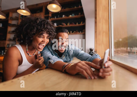 Junges Paar Zusammensitzen im Coffee Shop und nehmen Selfie mit Smartphone. Junger Mann und Frau lachen während der Einnahme von Selfie im café Stockfoto