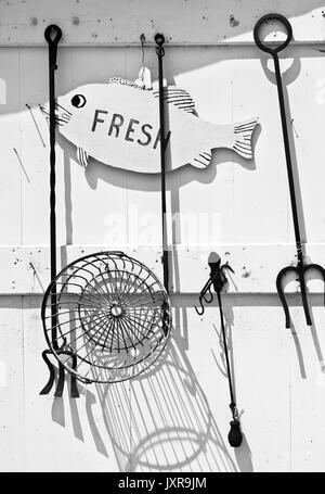 Vintage clamming Tools hängen an einer beunruhigten Wand im Neuenglischen Dorf am Meer. Holz- fisch Schild mit dem Wort "frisch". Schwarz-weiß-Bild. Stockfoto