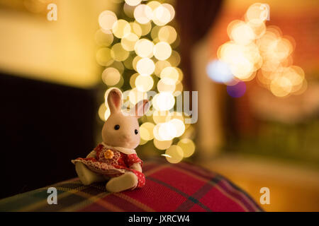 Sylvanian Familie toy Kaninchen in rot gepunkteten Kleid sitzt auf einem Sofa vor dem Weihnachtsbaum. Stockfoto