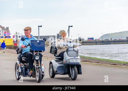 Largs, Schottland, Großbritannien. 17 August, 2017. UK Wetter: Zwei Menschen, deren Mobilität scooters entlang der Promenade und genießen Sie sonnige Abschnitte und gelegentlich schweren Duschen am Meer an der Westküste von Schottland. Credit: Skully/Alamy leben Nachrichten Stockfoto