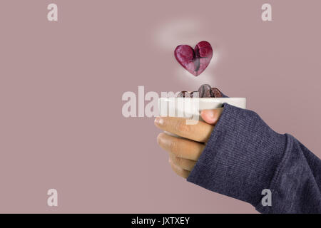 Die Hände einer Frau in einem Pullover mit einem Glas Kaffee Bohnen und rosa Herzen Kaffeebohne schwimmt über das Glas, Valentinstag und liebe Konzept. Stockfoto