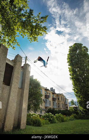 Stadt Parkour. Der Kerl macht das Gegenteil Salto. Sprung aus dem Gebäude. Aufnahmen aus der unteren Winkel. Geschicklichkeit und Extreme. Stockfoto