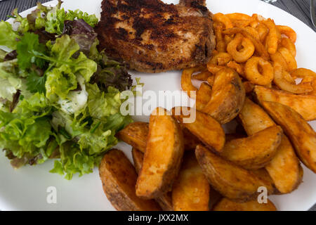 Schweinefleisch paniert mit gerösteten Kartoffeln Salat und Salat auf einem weißen Teller hacken. Stockfoto