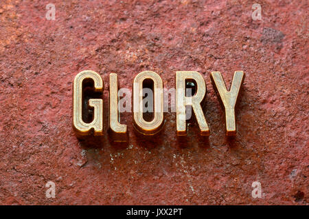 Herrlichkeit Wort von metallischen Buchstaben auf rotem rostige Oberfläche Stockfoto