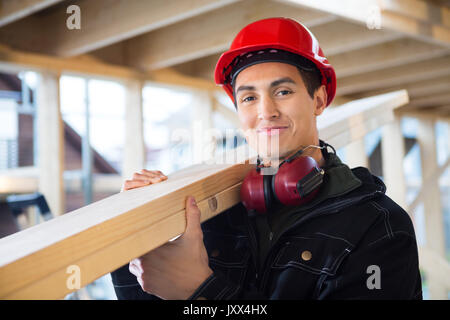 Tischler mit Holz auf Schulter auf der Baustelle Stockfoto