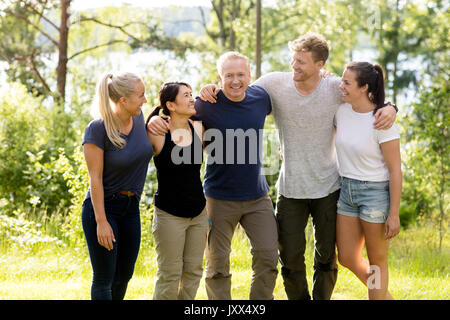 Mann mit verschränkten Armen um Freunde im Wald Stockfoto