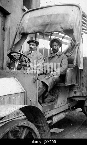 Sitzendes Porträt eines reifen afroamerikanischen Mannes, der raucht, und einer reifen afroamerikanischen Frau, beide mit neutralem Ausdruck, in einem Auto oder möglicherweise einem Maschinenstück, 1915. Stockfoto