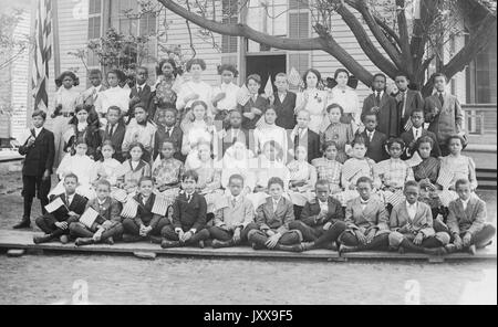 Ganzkörperbild von afroamerikanischen Schulkindern, alle in Uniform, die ersten drei Reihen sitzen, die vierte Reihe stehen, alle mit kleinen amerikanischen Fahnen, 1920. Stockfoto