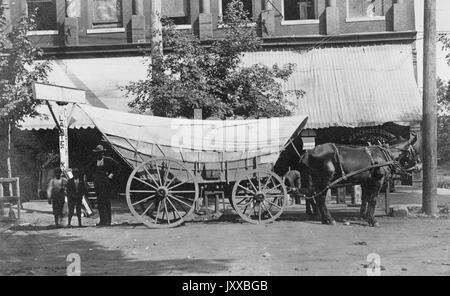 Ein afroamerikanischer Mann mit zwei afroamerikanischen Kindern, die neben einem Pferdewagen stehen, dunkle Kleidung und Hüte tragen, vor einem Geschäft stehen und Bäume auf einem Feldweg stehen, 1910. Stockfoto